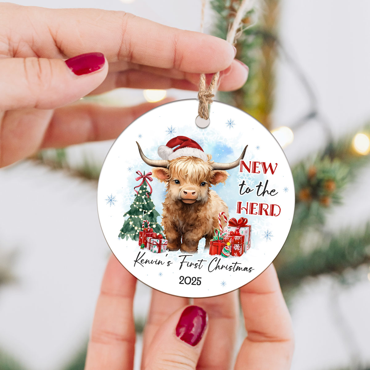 Custom Baby's First Christmas Ornament 2025 featuring a cute Highland cow in a Santa hat and red scarf, with Christmas tree, gifts, and text New to the Herd, customized with baby’s name.