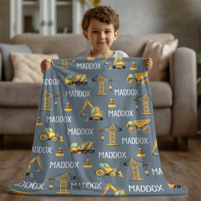 A Personalized Kid Name Blanket eaturing construction vehicles, customizable with different colors and names, is shown in a cozy living room.
